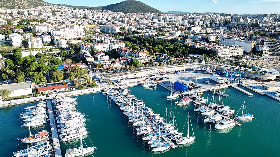 Kuşadası marina with sailing boats moored at the pontoons and the town spreading up the hillsides behind