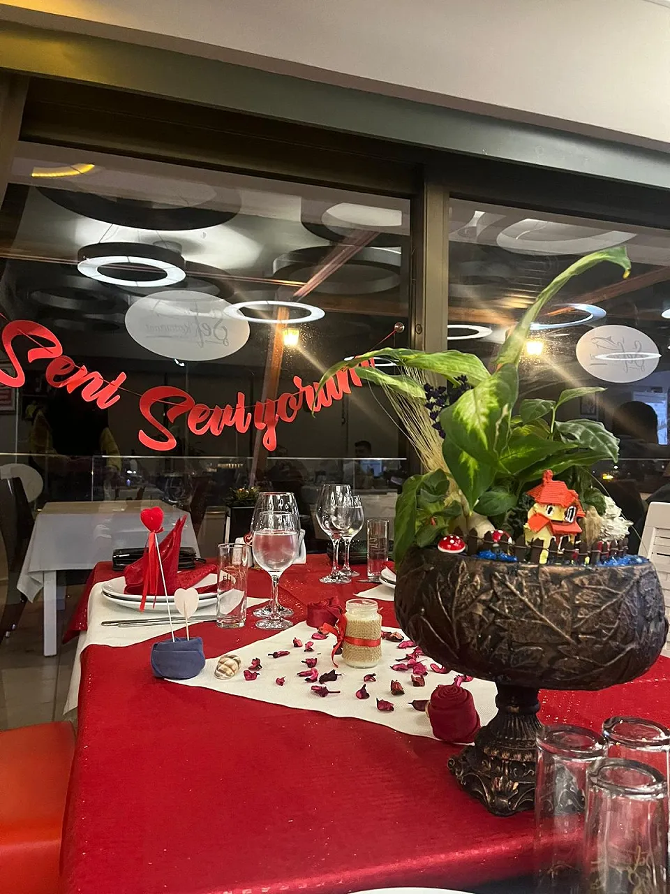 A romantic table decorated with a red tablecloth, rose petals and “Seni Seviyorum” (I love you) written on the glass