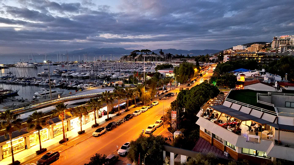The palm-lined seafront boulevard, the marina full of yachts and a building with a terrace on the right, at dusk