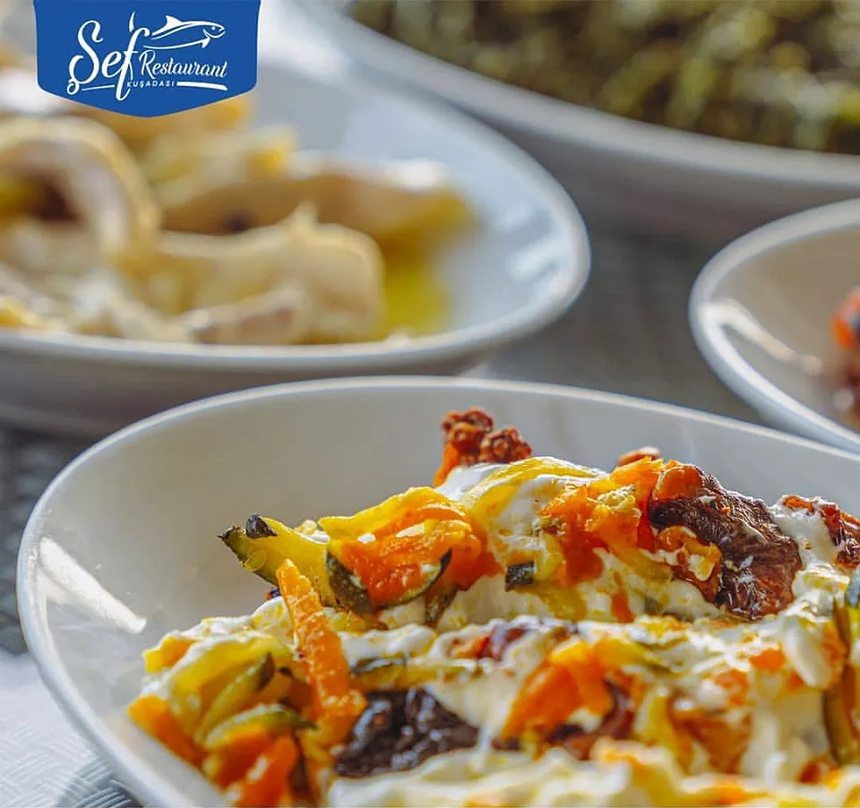 Fried vegetable meze drizzled with yoghurt and chilli flakes, with bowls of olive-oil meze behind