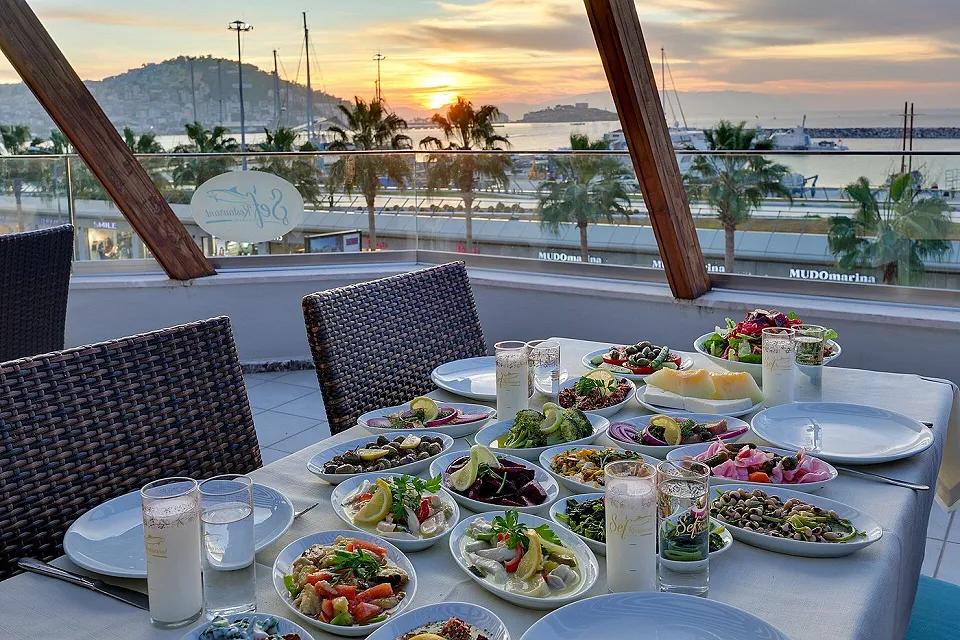 A table laid with rows of meze plates, and the sunset seen from the terrace in Kuşadası
