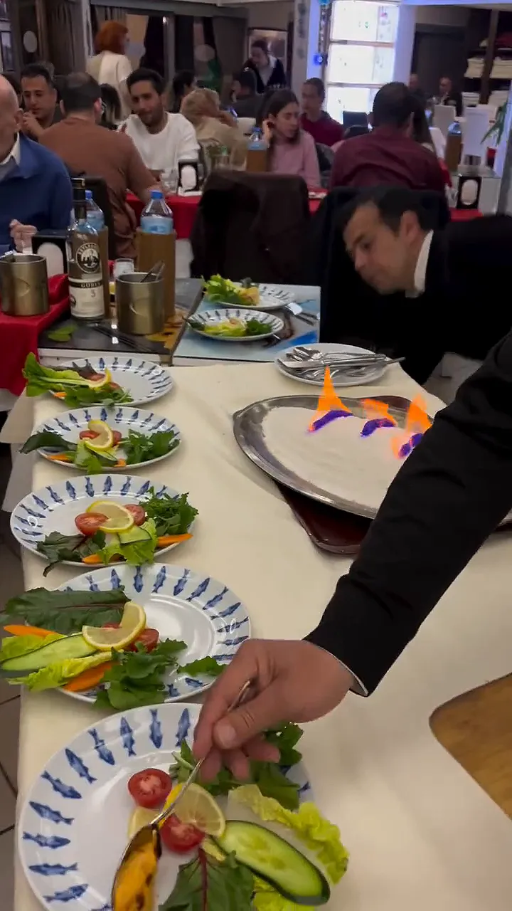 Video: a waiter serving salad plates beside a tray of salt-baked fish in flames